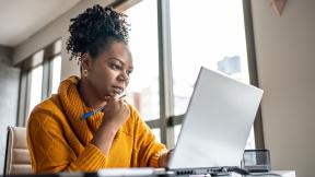 person sitting in office with hand on chin thinking while looking at laptop