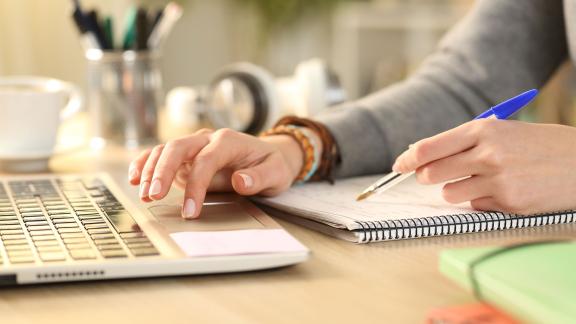 A homeworker making notes at a laptop.