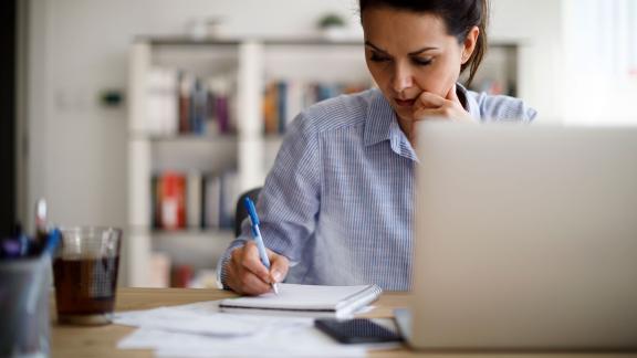 A homeworker makes notes next to their laptop.