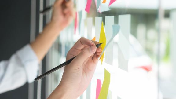Officer workers write on post-it notes stuck to a window.