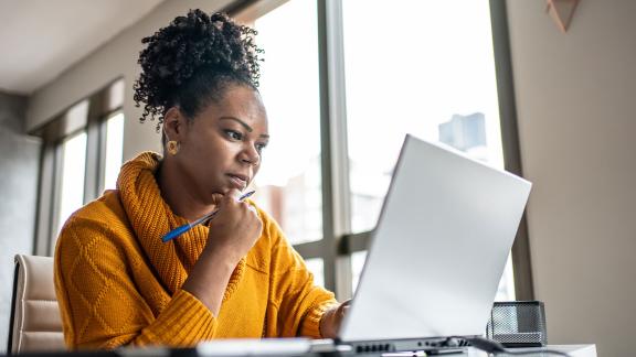 person sitting in office with hand on chin thinking while looking at laptop